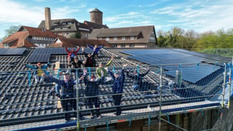 Teilnehmer des SolarCamps Kassel arbeiten auf einem Dach an einer Photovoltaikanlage, um die Energiewende voranzutreiben.