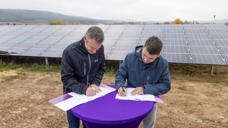 Stefan Zaubitzer (links) und Bürgermeister André Gölitzer unterzeichnen vor Solarmodulen einen Vertrag zur Photovoltaikanlage.