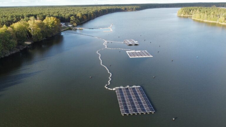 Luftaufnahme eines Sees mit schwimmenden Photovoltaikanlagen, die im Rahmen eines Forschungsprojekts installiert wurden.