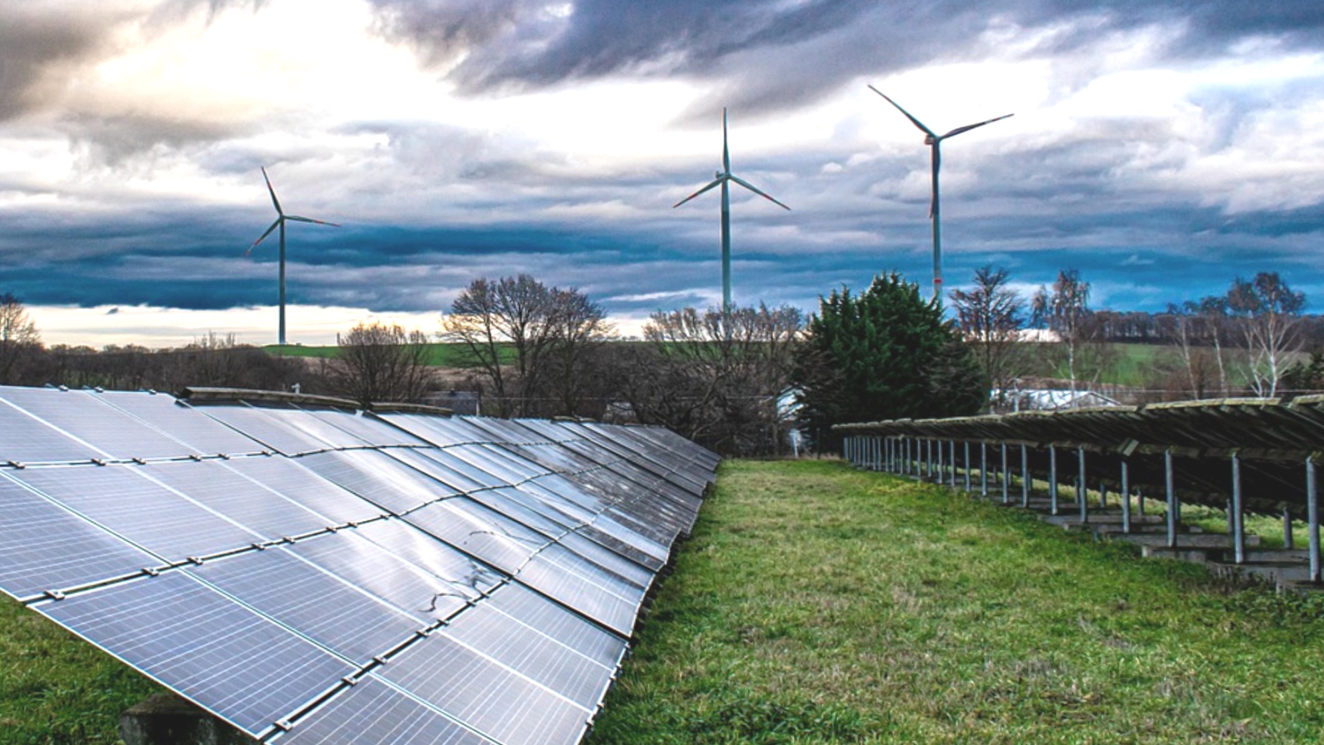 Solarpark mit Photovoltaikanlagen und dahinter aufragende Windturbinen als Symbol der Energiewende