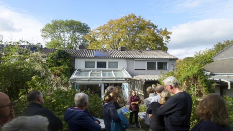 Teilnehmende einer Solarparty blicken auf ein mit Photovoltaik-Modulen ausgestattetes Haus in der Nachbarschaft.