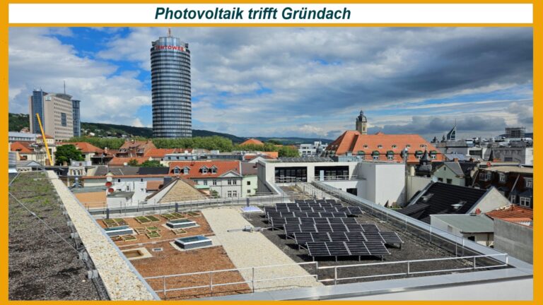 Das Bild zeigt das Bürgeramt in Jena mit einem begrünten Dach, auf dem teilweise Photovoltaik-Module installiert sind. Die Solarmodule sind in die Dachbegrünung integriert, um Sonnenenergie zu erzeugen und gleichzeitig das Stadtklima zu verbessern. Das Gebäude liegt zentral in der Innenstadt, gut sichtbar in der Nähe des markanten Jena-Towers. Die Kombination aus Gründach und Solarstromversorgung verdeutlicht moderne, nachhaltige Stadtplanung, bei der ökologische und energieeffiziente Lösungen in öffentlichen Gebäuden umgesetzt werden, um langfristig CO₂-Emissionen zu reduzieren und Energie zu sparen.