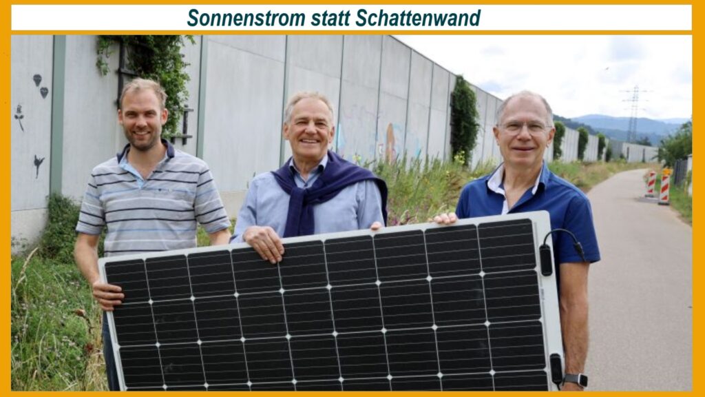 Mitglieder der Bürgerenergiegenossenschaft Ortenau stehen gemeinsam vor einer Lärmschutzwand, auf der demnächst Photovoltaikmodule installiert werden. Sie halten ein Solarmodul gemeinsam hoch und präsentieren damit das von der Genossenschaft selbst finanzierte Projekt. Die Gruppe lächelt in die Kamera, während die Wand im Hintergrund sichtbar ist. Dieses Bild symbolisiert gemeinschaftliches Engagement für erneuerbare Energien in der Region Ortenau und den erfolgreichen Einsatz von Bürgerbeteiligung zur Förderung nachhaltiger Energieprojekte vor Ort.